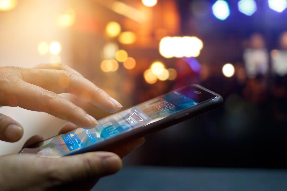 Hand bedient Mobiltelefon vor leuchtendem Hintergrund.