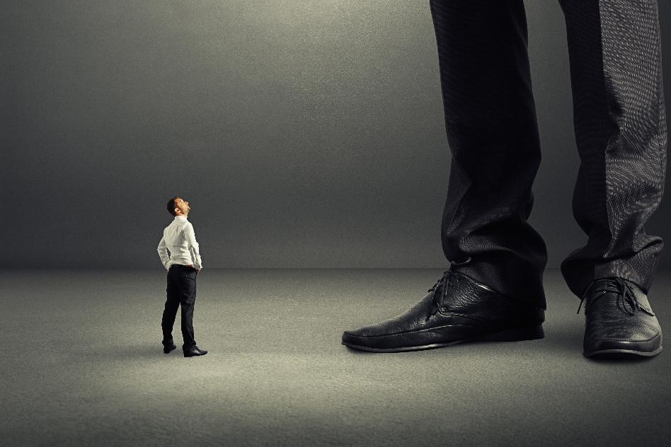 kleiner Mann steht neben überdimensional großem Mann, von dem nur Hosenbein und Schuhe zu sehen sind.