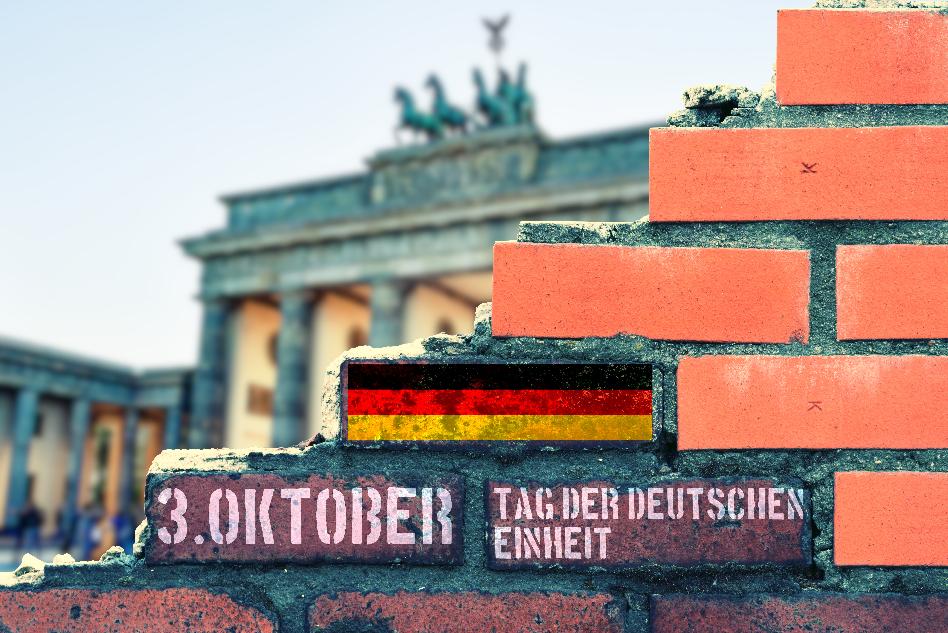 Mauerteile vor Brandenburger Tor. Auf der Mauer ist eine deutsche Flagge abgebildet, das Datum 3. Oktober und der Satz 