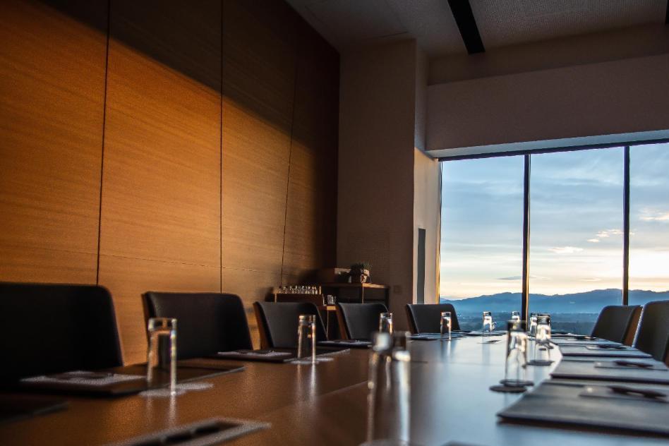 Leerer Konferenzraum mit Tisch und Stühlen, im Hintergrund ein großes Fenster mit Blick in den Himmel